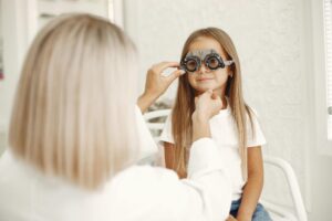 A young girl getting an eye exam at a healthcare clinic with optometrist assistance.